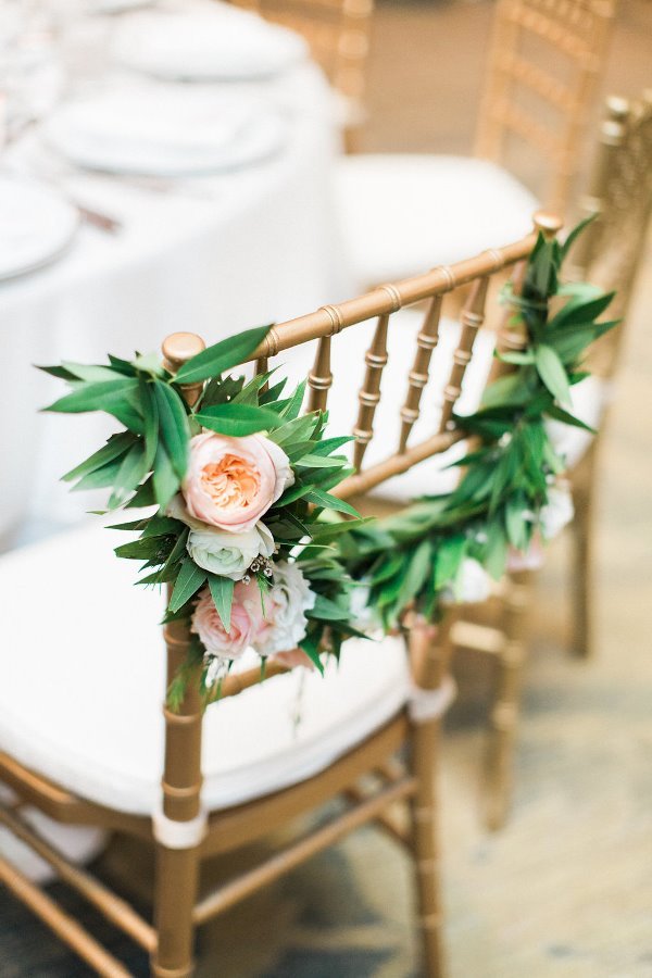 Decorated gold Chiavari chair with pink and white flowers and green leaves, at a white table set for a formal event.