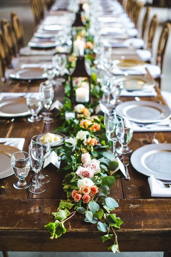 A long wooden banquet table decorated with a floral centerpiece, candles, and elegant tableware for a formal event or celebration.