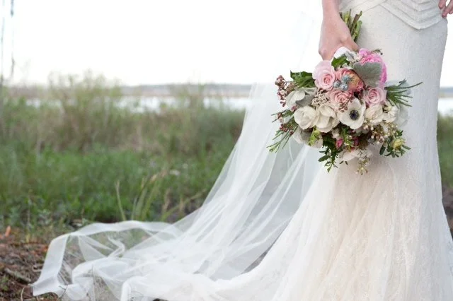 Close-up of a bride holding a pink and white bouquet in an outdoor setting.