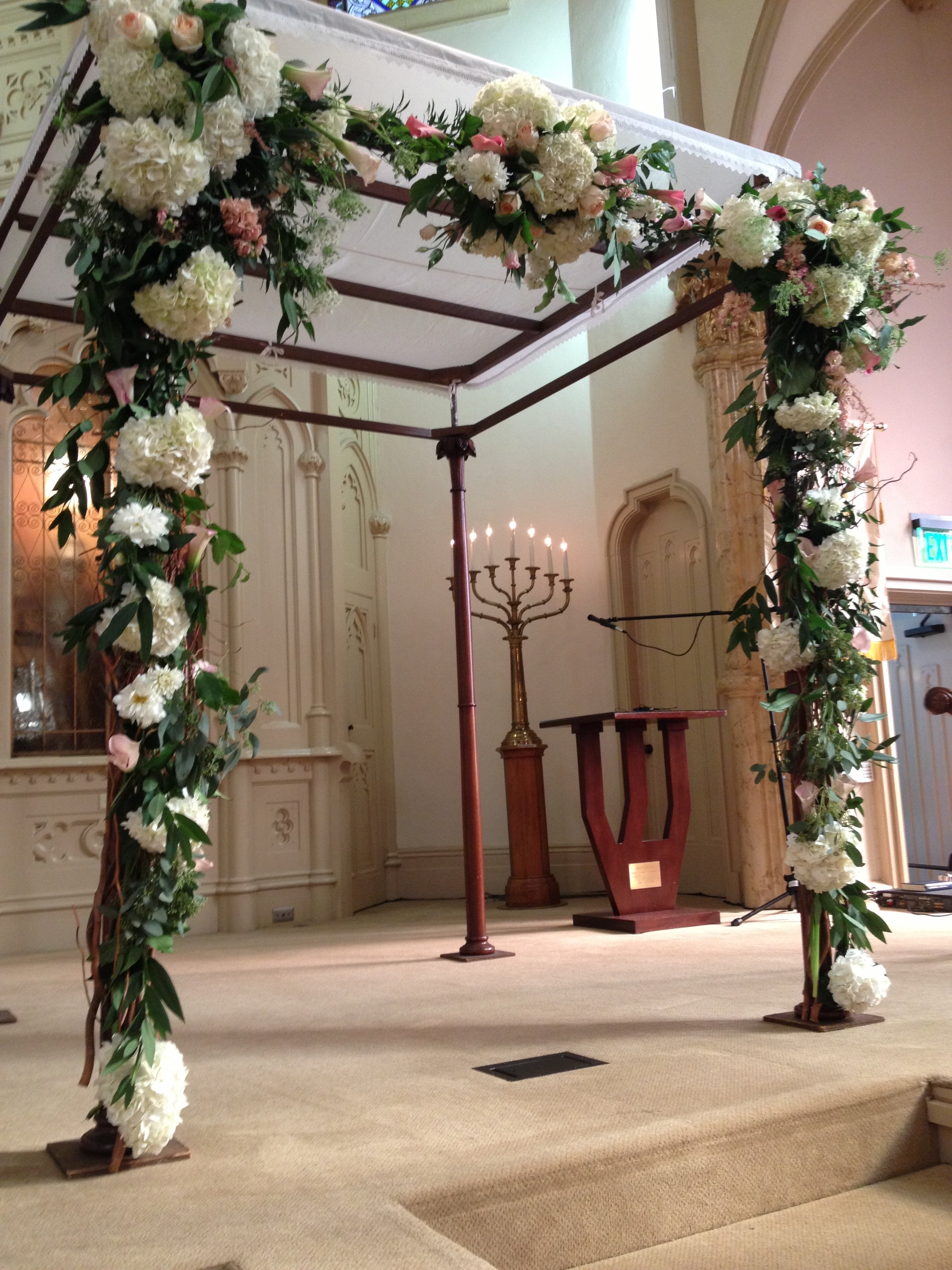 Wedding altar decorated with a flower arrangement of white and pink flowers and greenery, set on a wooden structure inside a church.