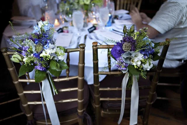 Close-up of two decorated chairs with floral arrangements at a dining table, a wedding or special event setting.