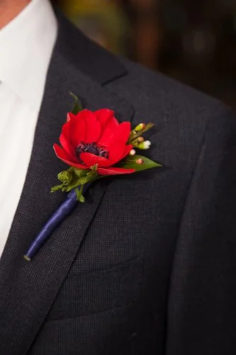 A red flower boutonniere pinned to a dark suit jacket