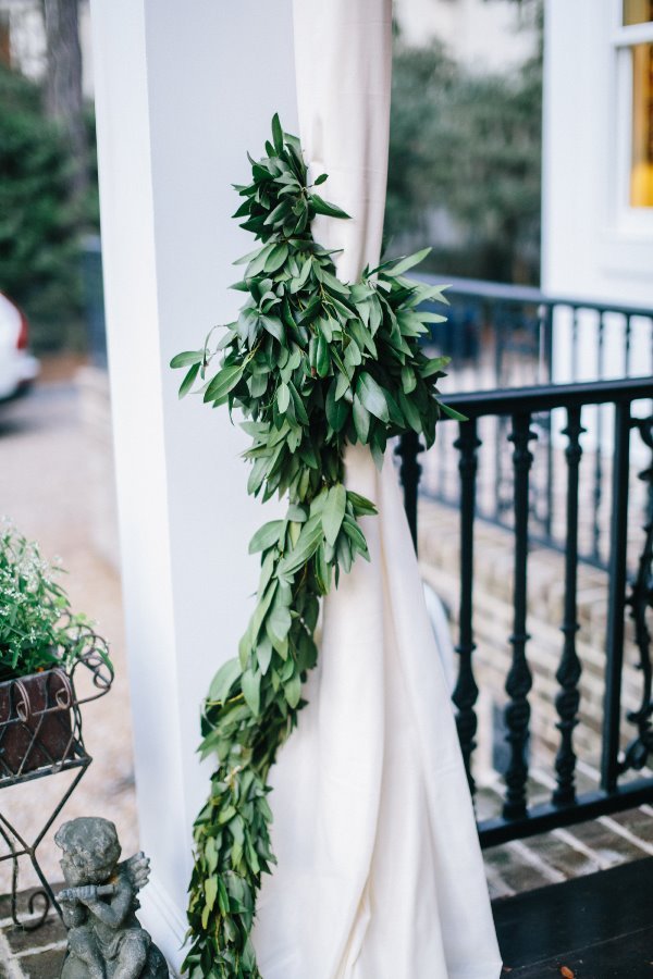 Green leafy garland draped around a white curtain on a porch with a black railing.