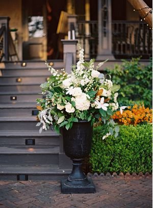 Large floral arrangement of white and green flowers in a black urn on a sidewalk