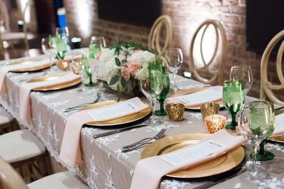 Elegant table setting with floral centerpiece, gold-accented plates, pink napkins, and wine glasses, in a warmly lit dining area.