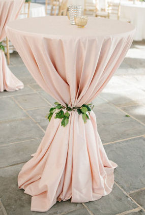 A table covered with a pink tablecloth tied with a green leafy ribbon.
