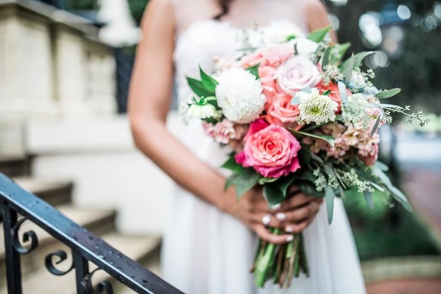 Bride holding a bouquet of pink, white, and blush flowers on a porch staircase.
