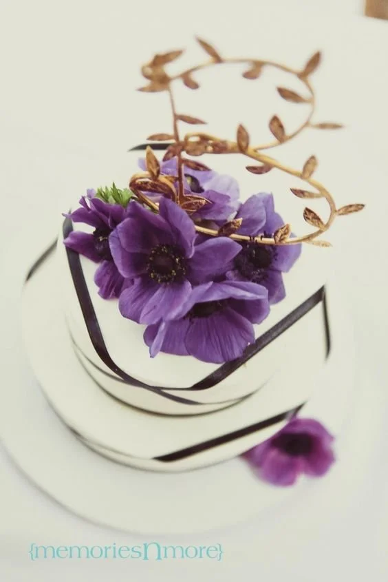 A white cake decorated with purple flowers and chocolate curls.