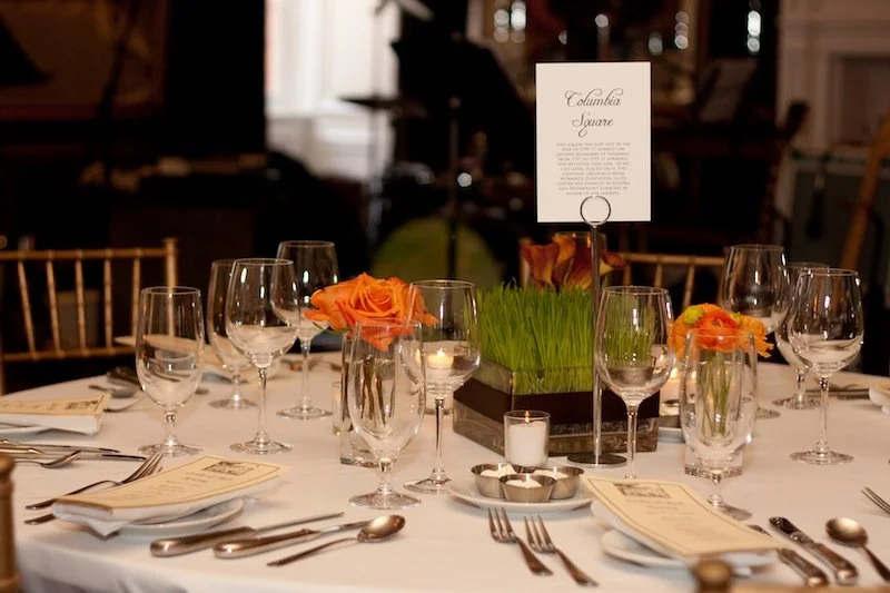 Elegant banquet table setup with wine glasses, water glasses, floral centerpieces, candles, and place settings in a formal dining venue.