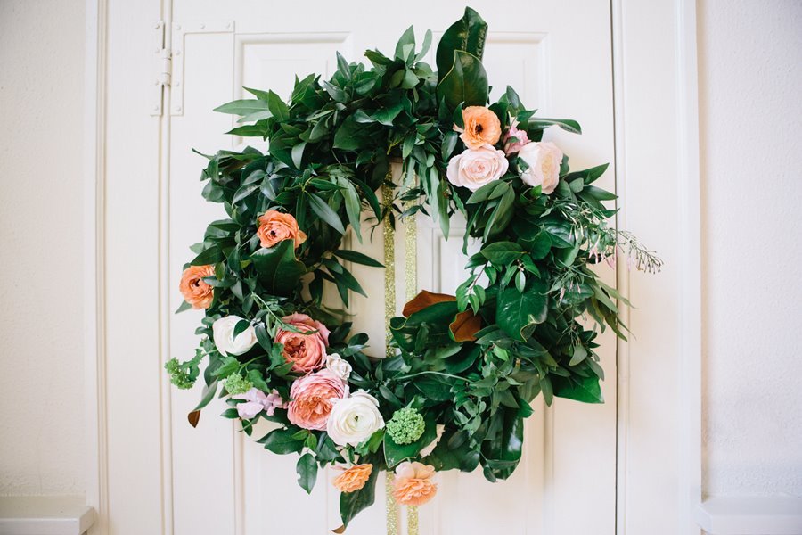 Decorative floral wreath hanging on a white door, featuring pink, white, and peach flowers with green foliage.