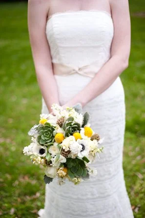 A woman in a white strapless dress holding a bouquet of flowers outdoors.