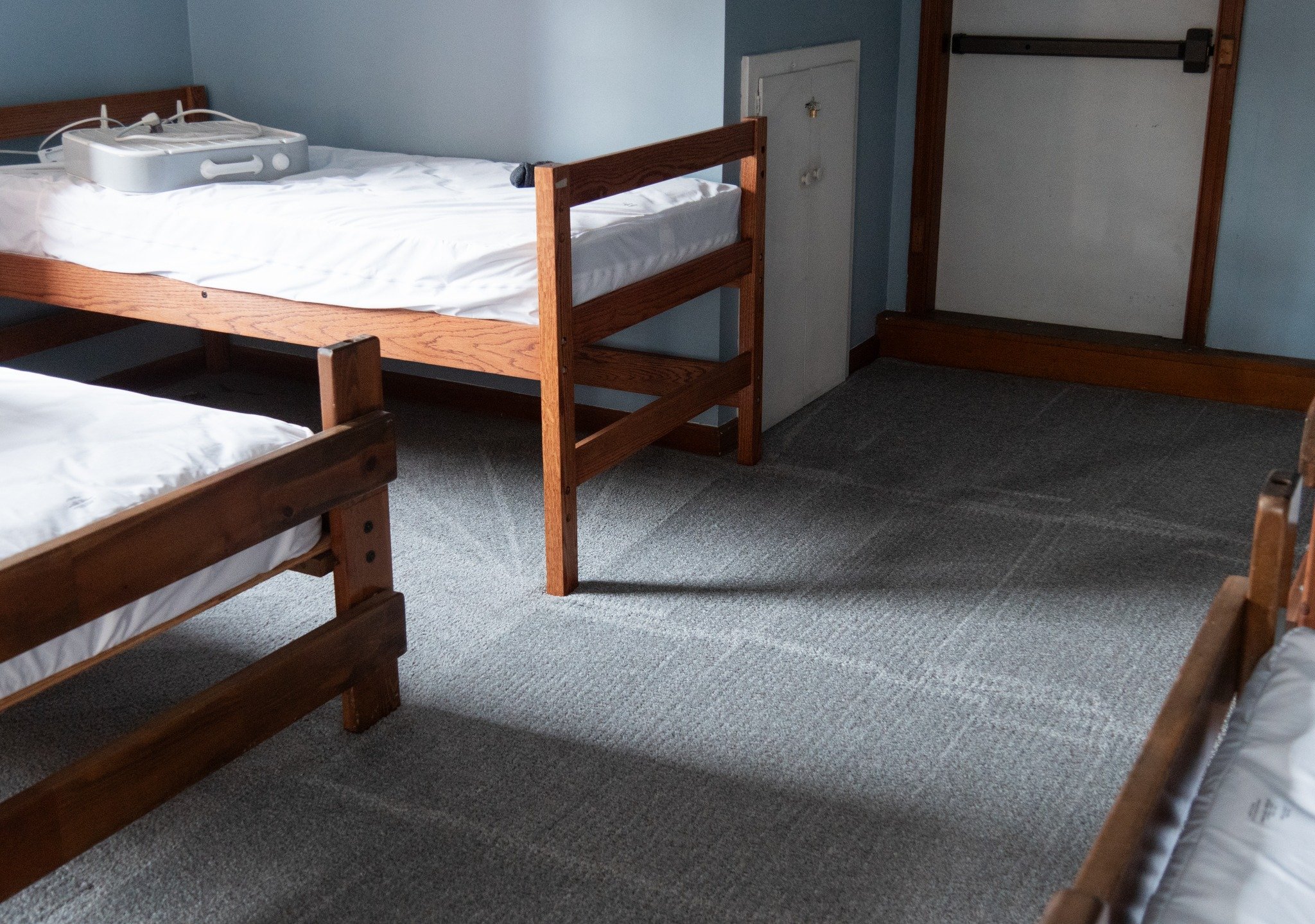 Three wooden bunk beds with white linens in a room with blue walls and gray carpet.