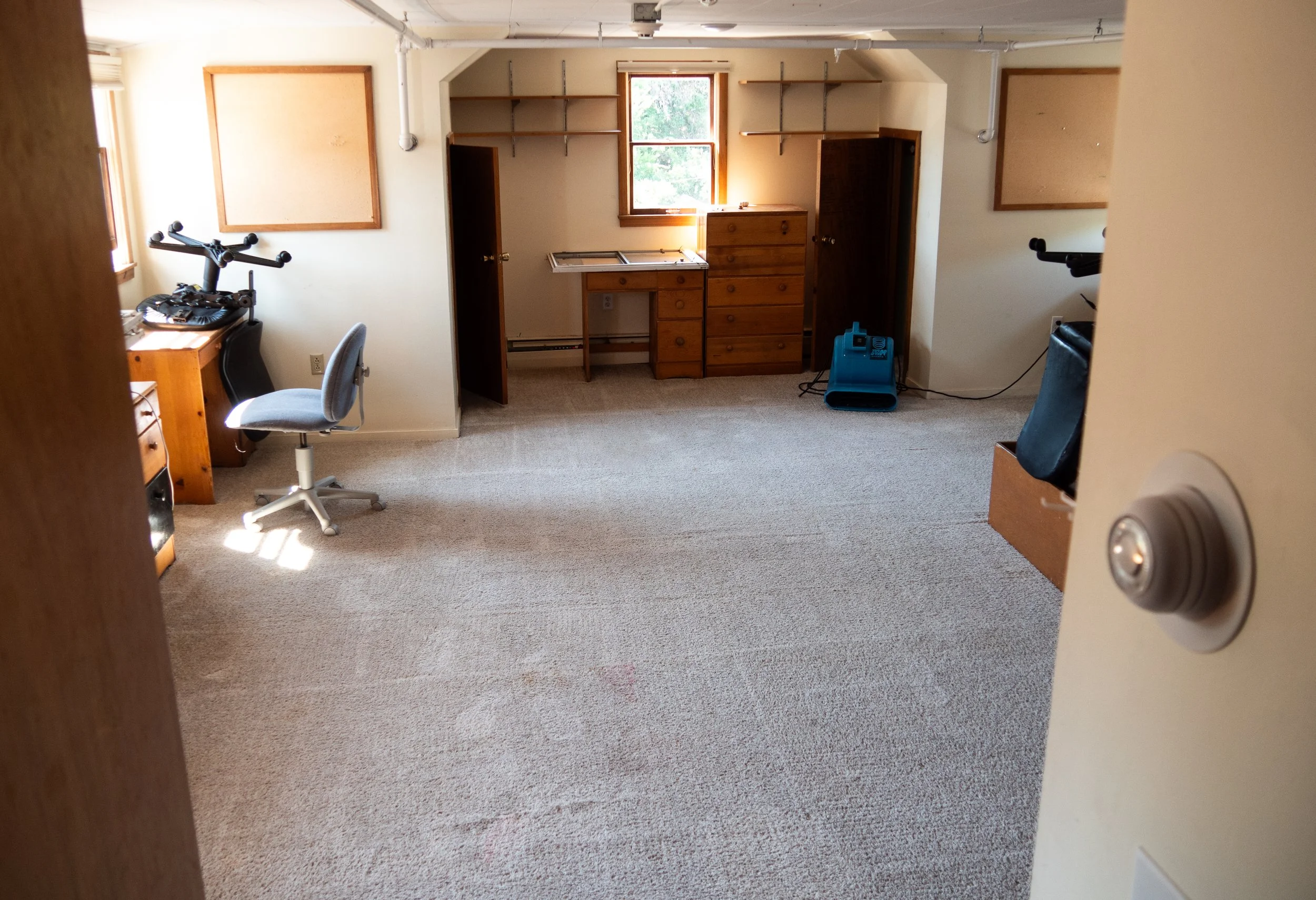 A room with beige carpet, two windows, wooden furniture, and some electronic equipment, viewed through an open door. Removing stubborn dirt and allergens from bedroom carpets in Big Sky.