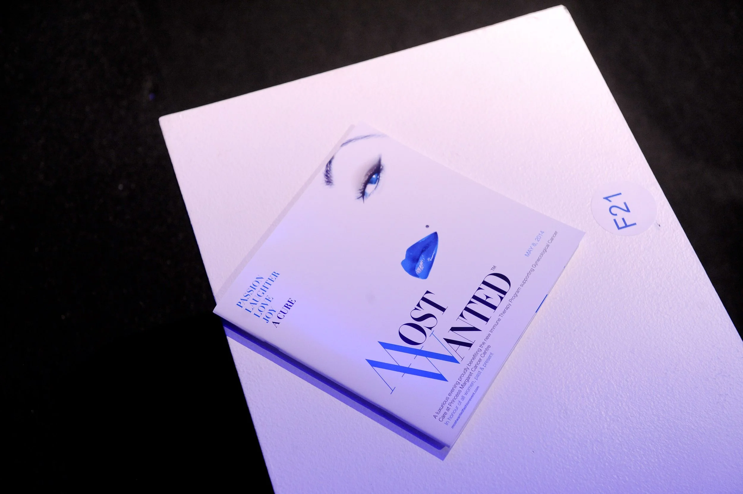 Closed white pamphlet featuring a blue lipstick and stylized eye illustration, with the title 'Most Wanted' and the subtitle 'A Cure'.