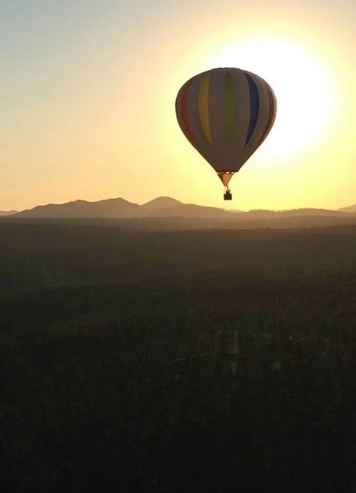 A hot air balloon floating in the sky during sunrise with mountains in the background.