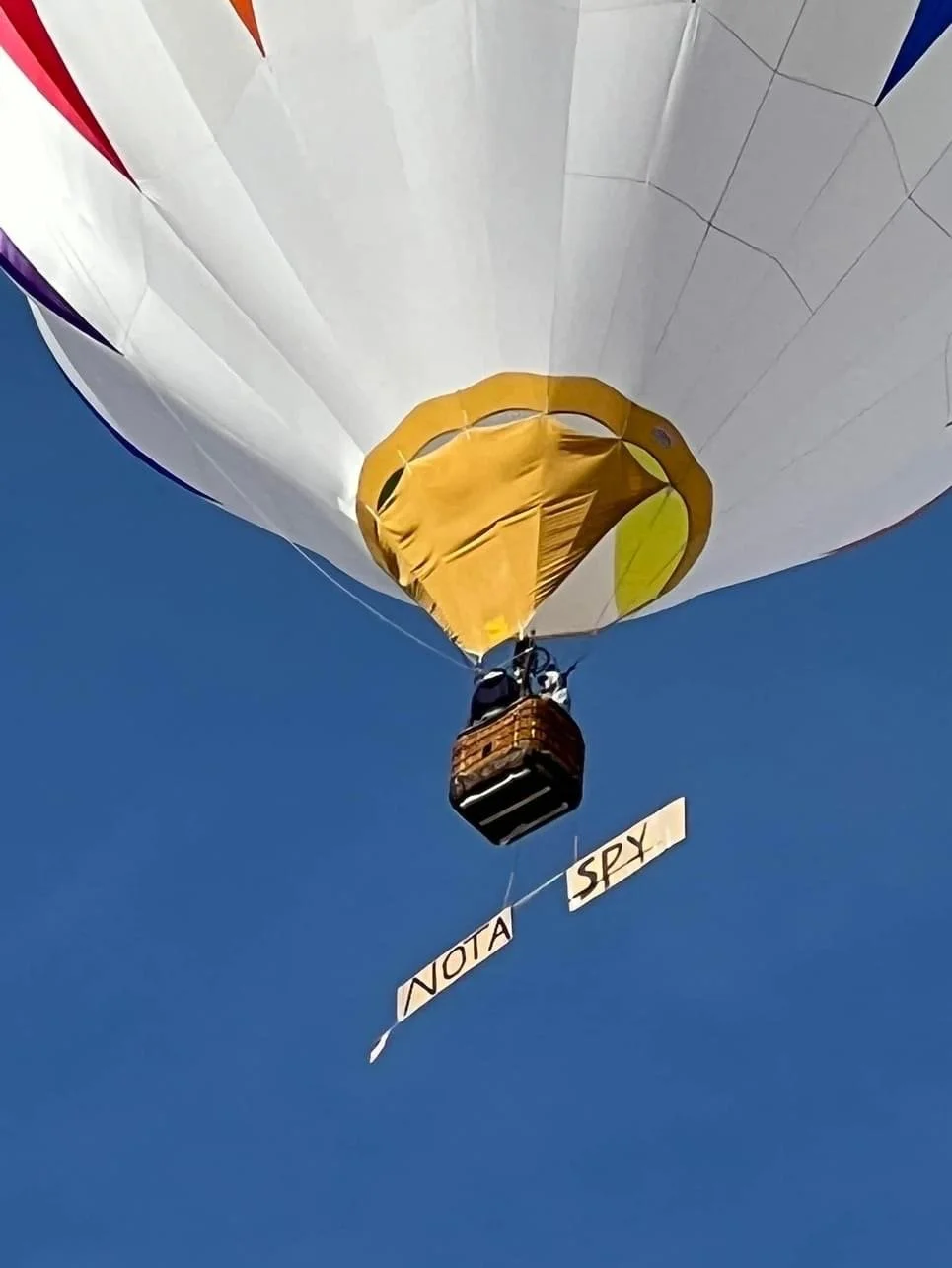 A hot air balloon with the words 'NOT A SPY' hanging beneath the basket to roughly represent a solar panel of a Chinese spy balloon against a clear blue sky.