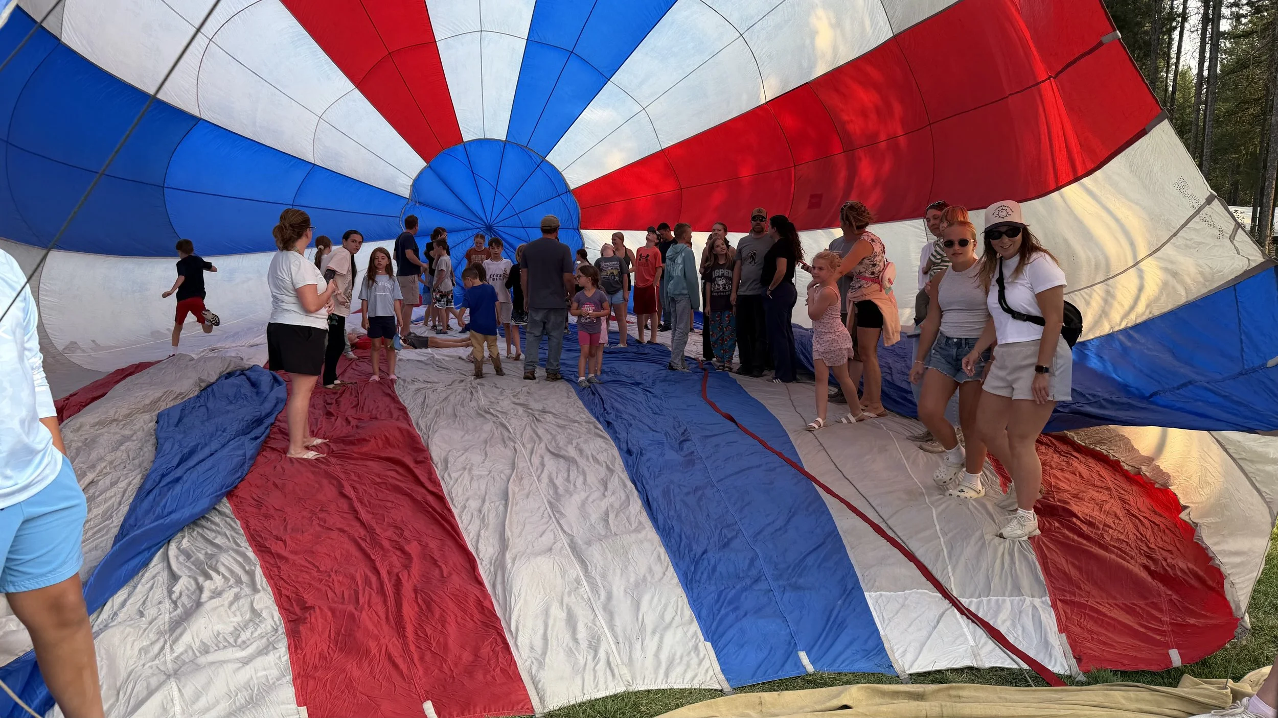 Group of people, including children and adults inside a large red, white & blue hot air balloon.