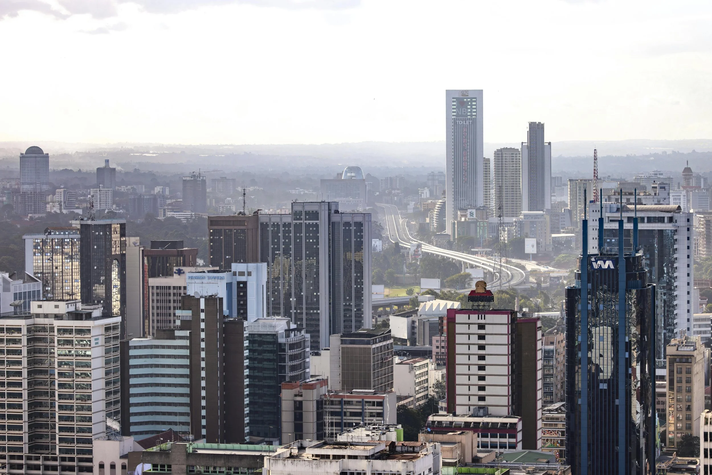 A city skyline with multiple tall buildings, highways, and skyscrapers under a cloudy sky.
