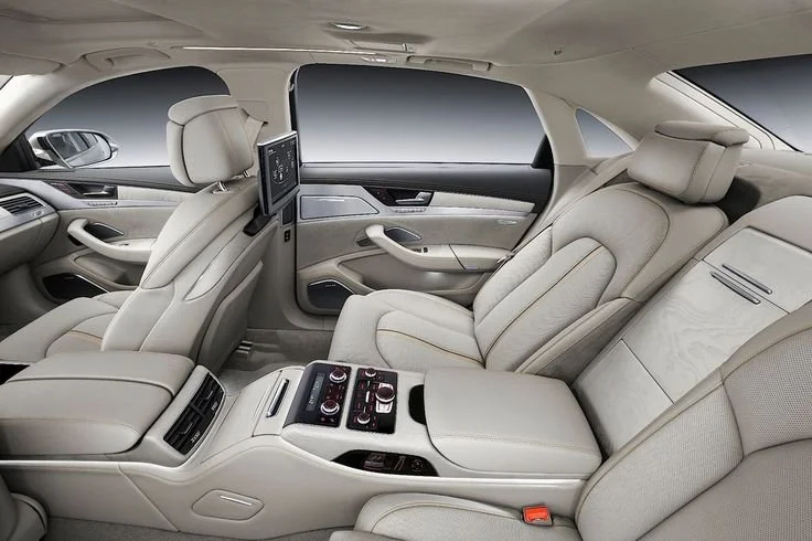 Interior of a luxury car showing beige leather seats, a center console with controls, and a headrest-mounted screen.