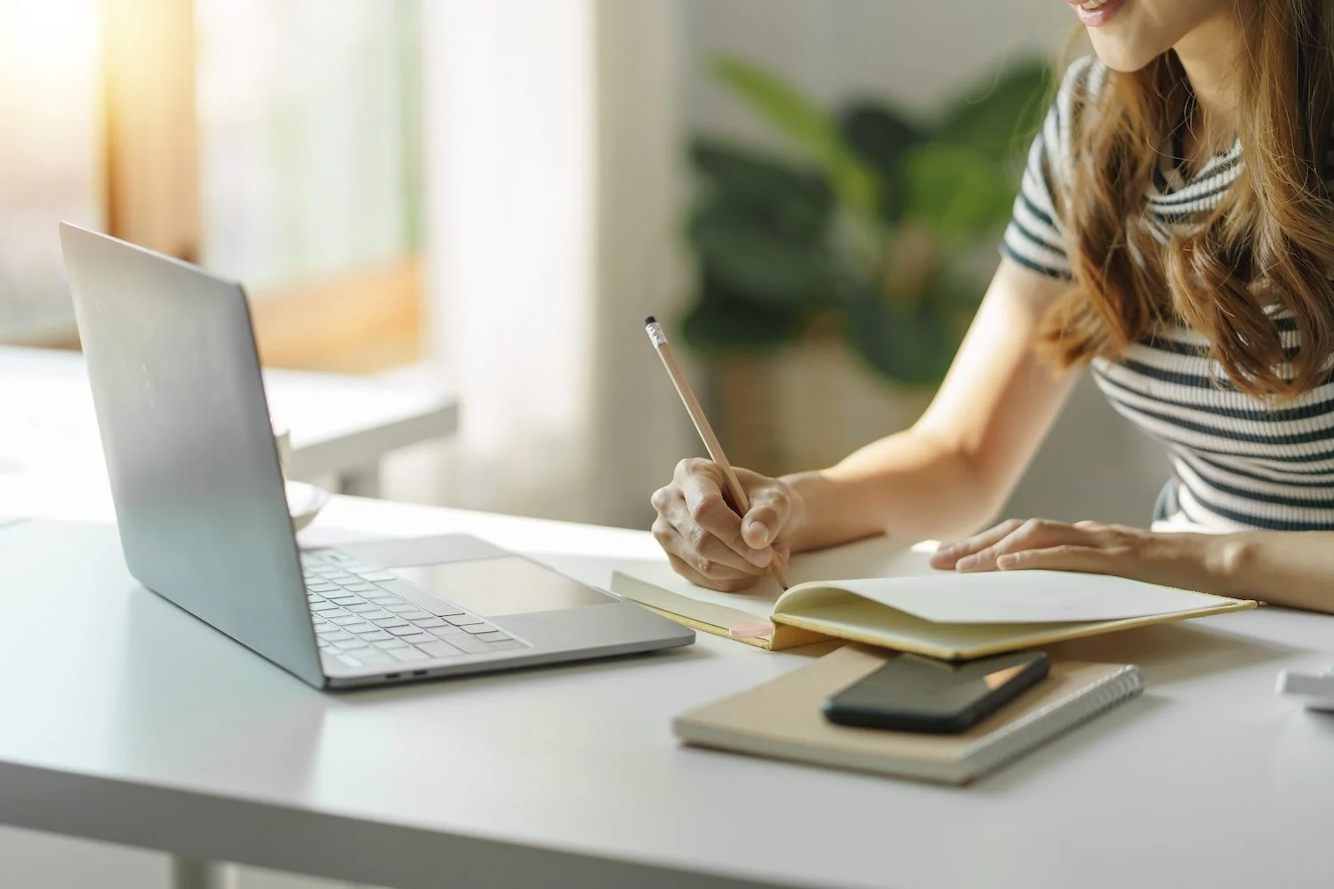 Person taking notes in a notebook beside a laptop while studying or completing online coursework