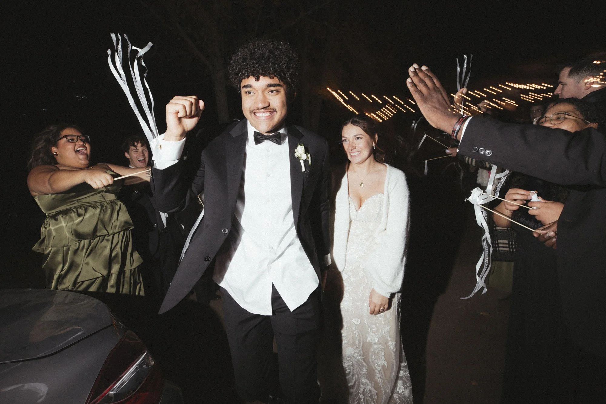 flash photo of bride and groom exiting their reception with friends cheering and waving streamers