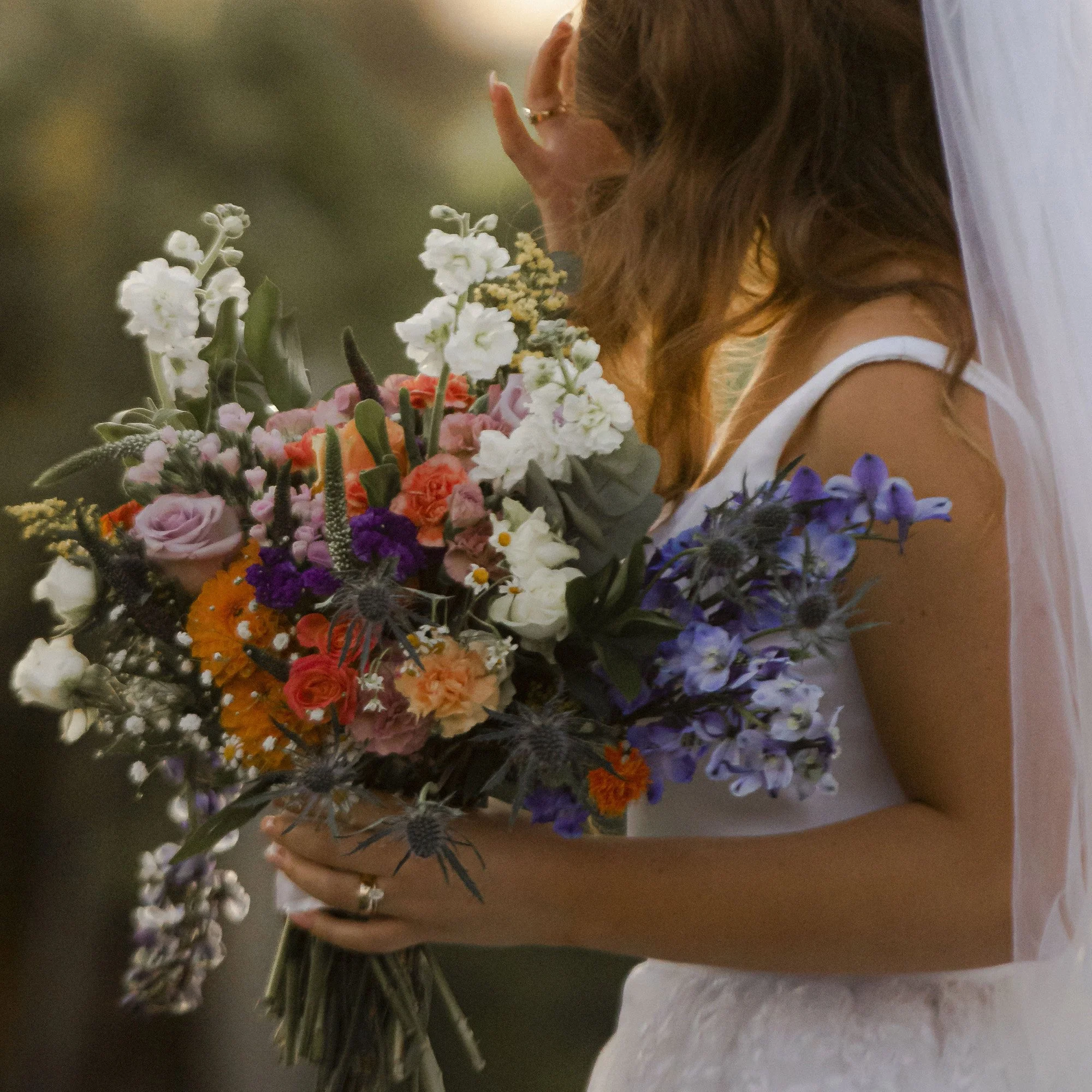 bride holds her colorful bouquet of purple, white, orange, and red and pink flowers