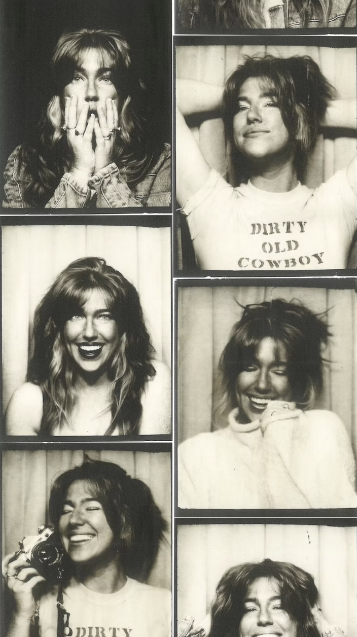 Black and white photo booth strip with six pictures of a young woman with messy, shoulder-length hair and a playful, happy demeanor, wearing casual clothing, including a T-shirt with the words "DIRTY OLD COWBOY." She is making different facial expressions and poses in each photo, sometimes covering her face, smiling, or holding a camera.