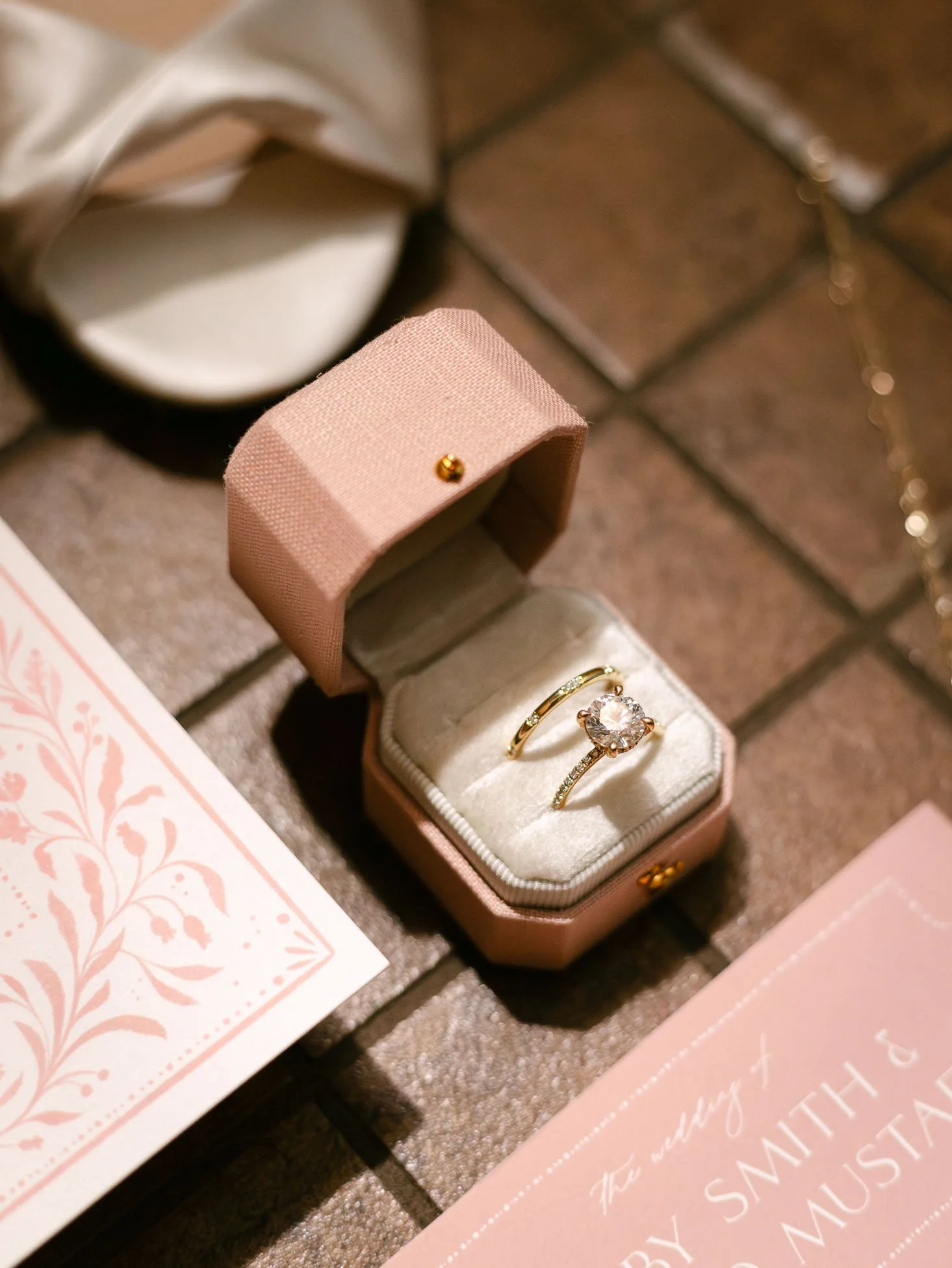 pink ring box on the floor holds a round diamond ring set in gold