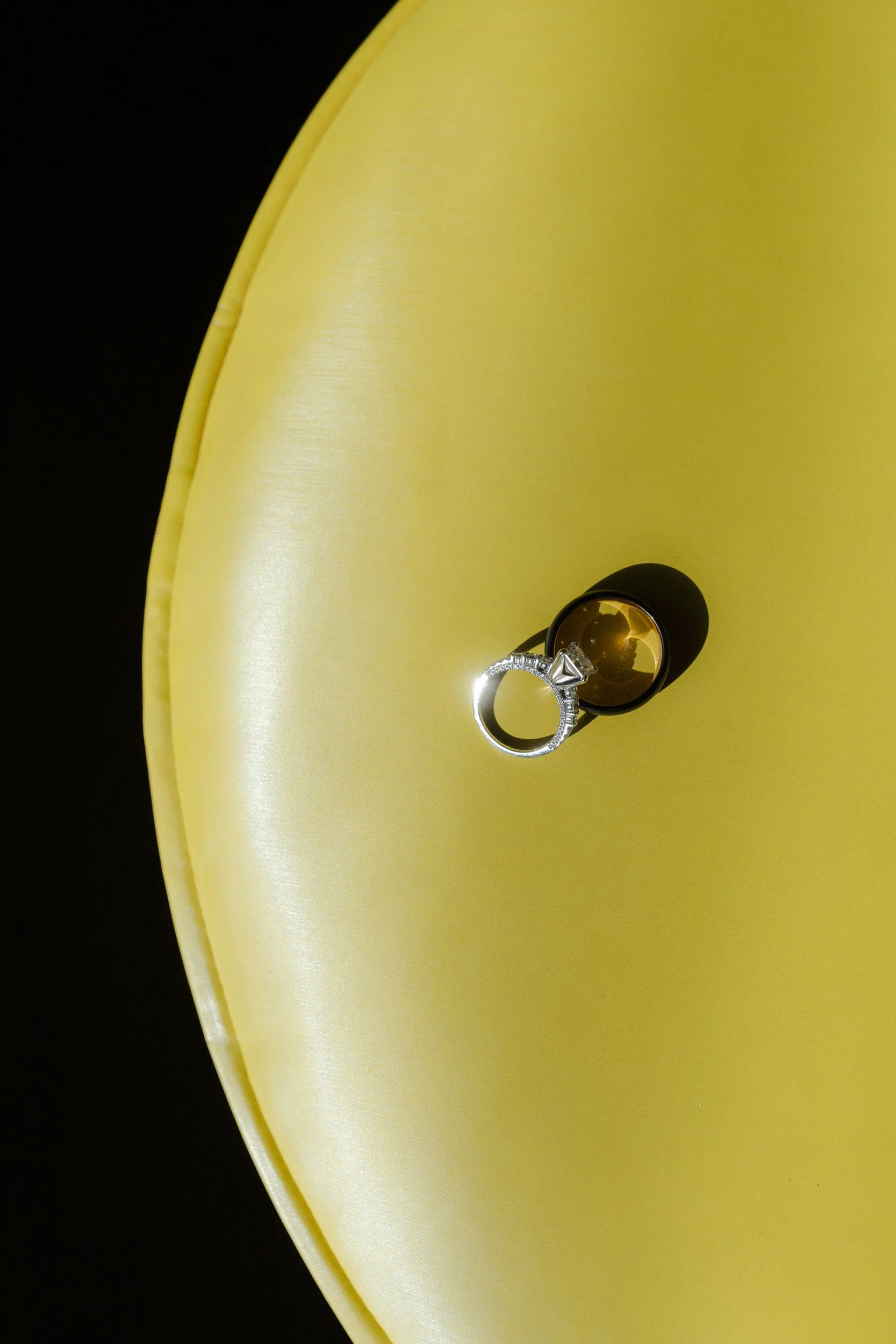 a black ring and a silver engagement ring on a bright yellow rounded leather seat