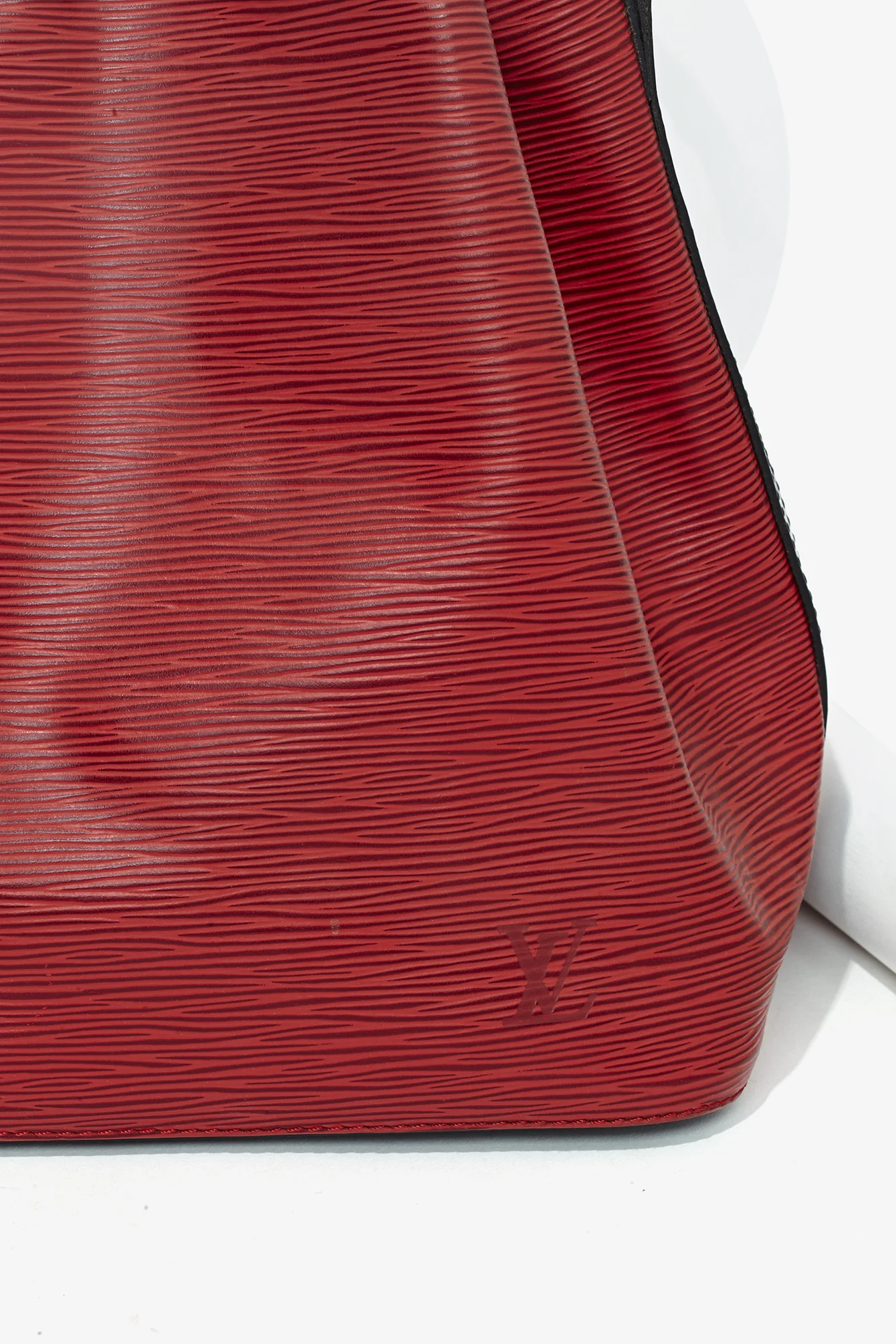 Close-up of a red Louis Vuitton bag with black edges, showing the textured leather surface with the LV logo. e-commerce, editorial, fashion, vogue