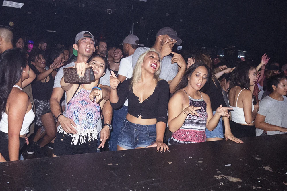 Crowd of people enjoying a night out at a music venue, dancing and taking photos.