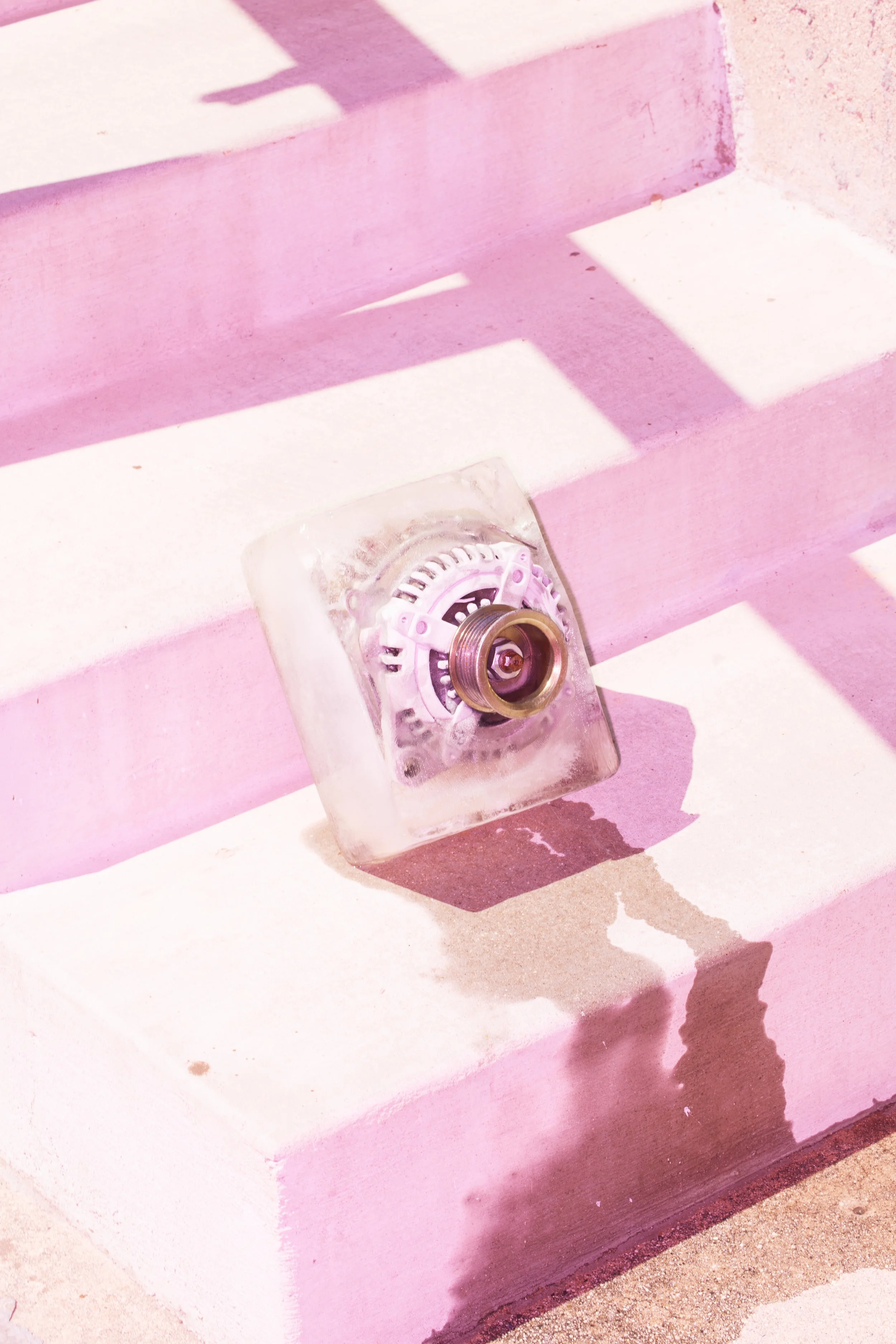 Close-up of a frosted glass firefighter helmet resting on a white and pink painted concrete step, with shadows cast by the sunlight.