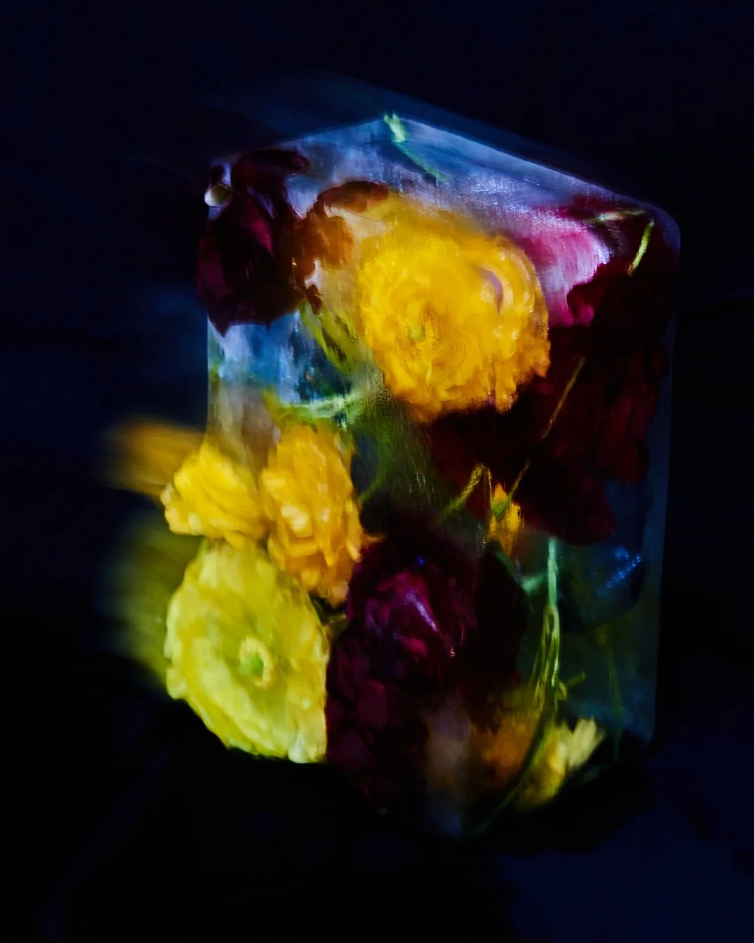 Illuminated glass vase with a colorful assortment of flowers including yellow, orange, red, and purple blooms, against a dark background.