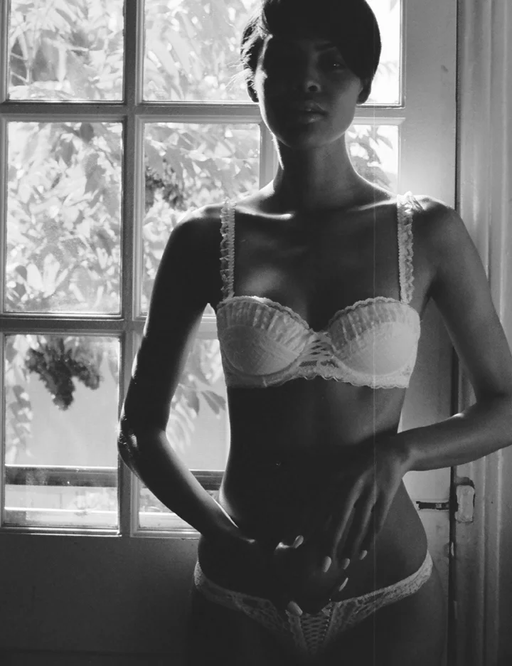 A woman standing in front of a window in lingerie, with sunlight behind her.
