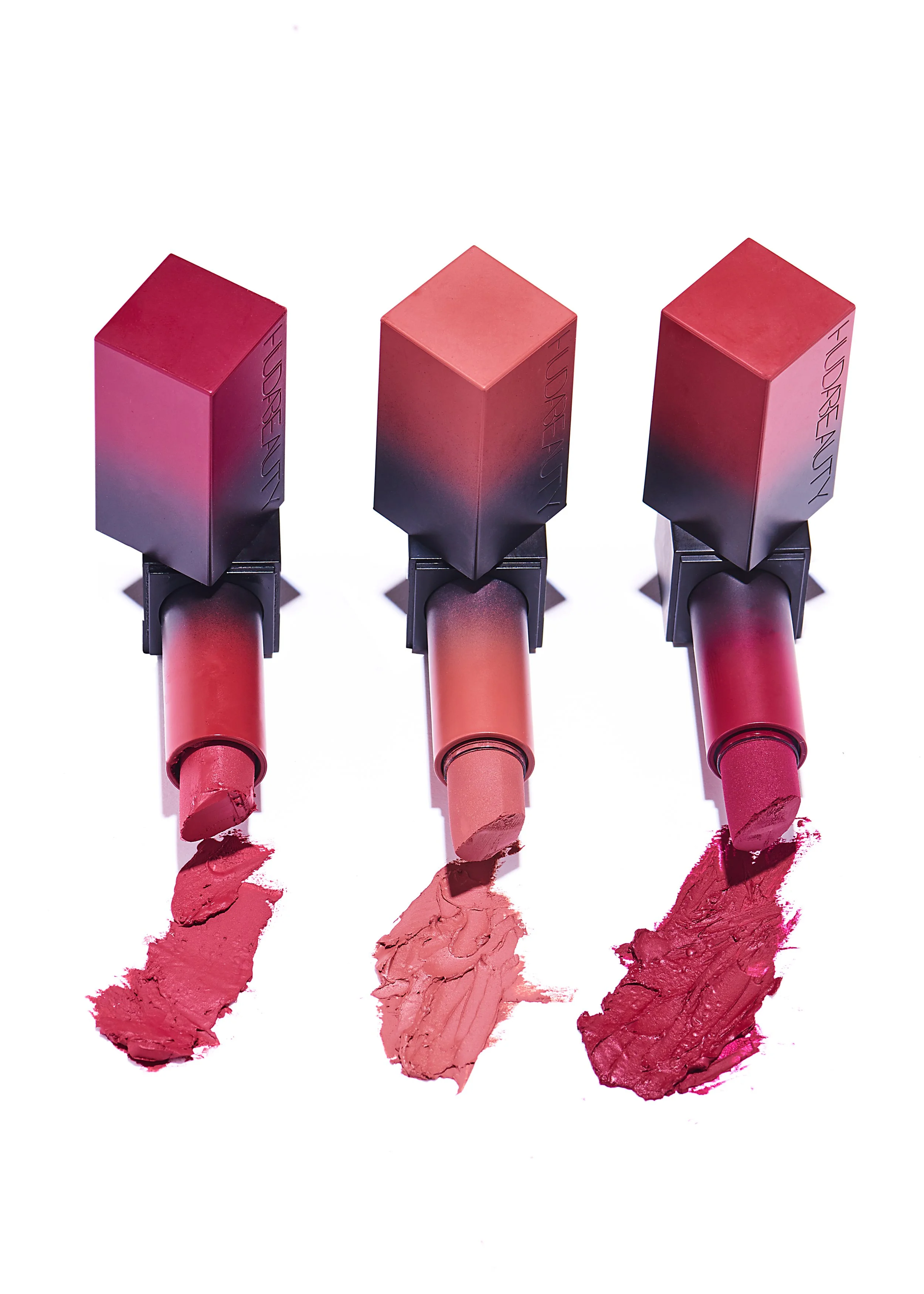 Three tubes of pink and red lipstick with swatches of lipstick color on a white background.