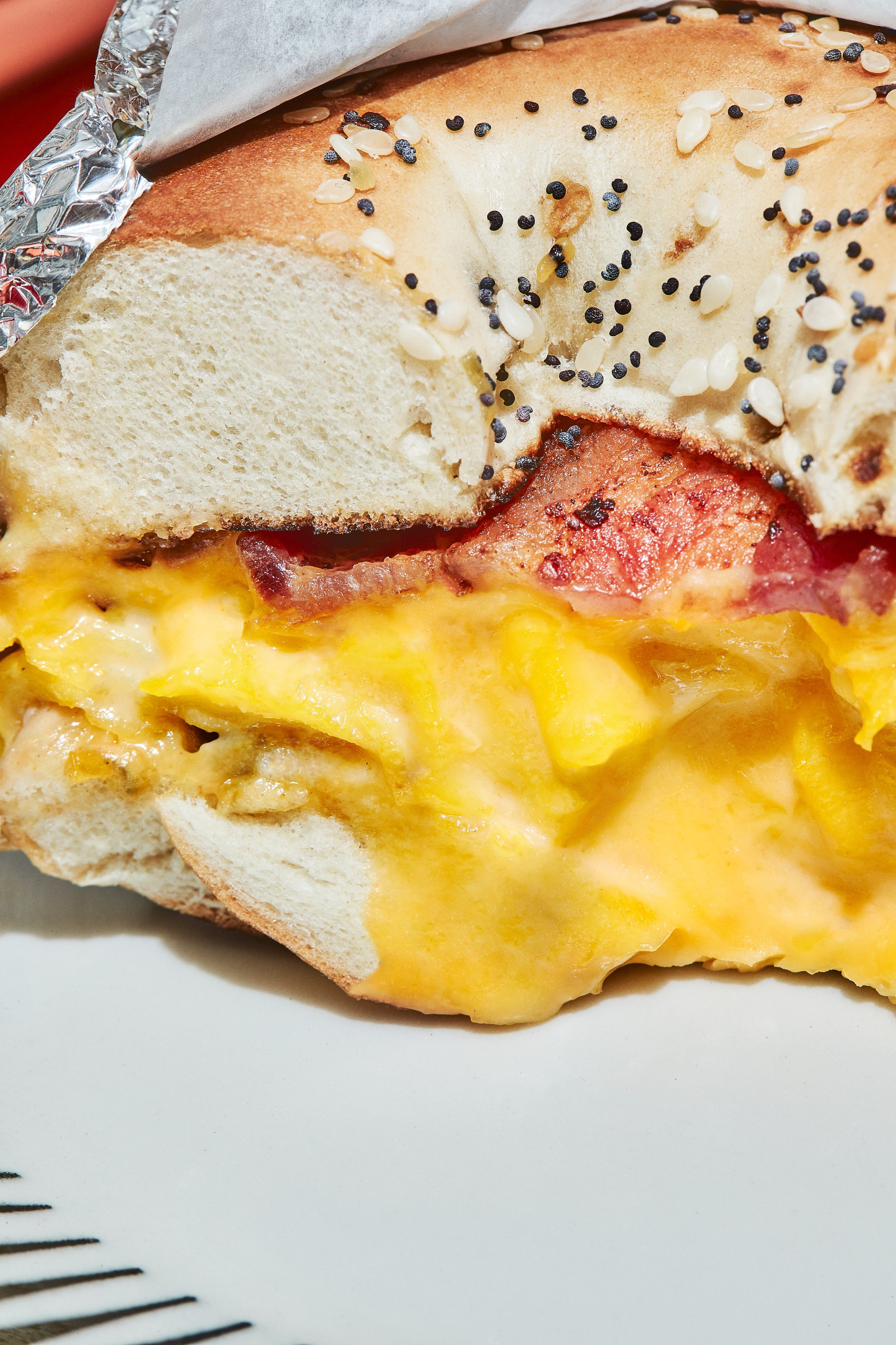 Close-up of a breakfast sandwich with scrambled eggs, bacon, and cheese on sesame seed bagel.