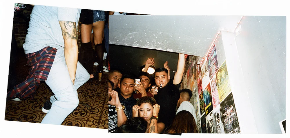 Group of young adults at a nightclub or party, some holding drinks, with a wall decorated with posters behind them.