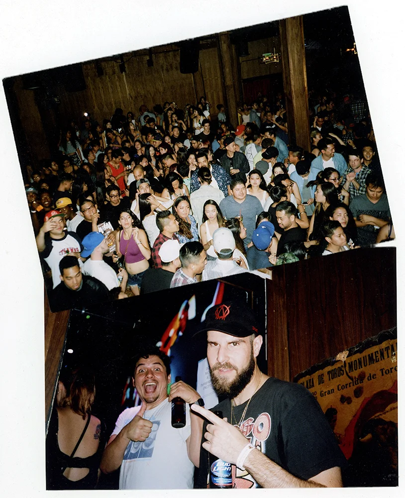 Crowd of people at a concert or party, with two men in the foreground making gestures for the camera, one holding a microphone and the other pointing.