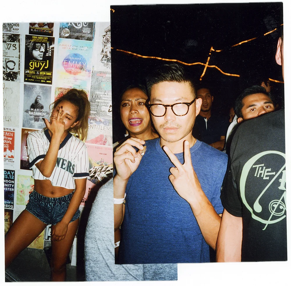 A group of people at a party, with a woman on the left appearing to yawn or stretch, and three individuals in the center posing for the camera, making peace signs or gestures.