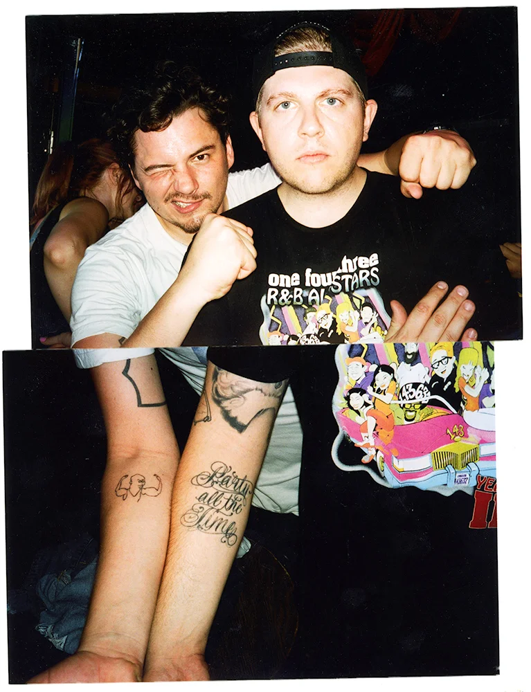 Two young men posing together at a social event. The man on the left has dark hair, is winking, and making a fist with his right hand. The man on the right has light hair, is wearing a backward cap, and has his fists raised. The bottom part of the ph