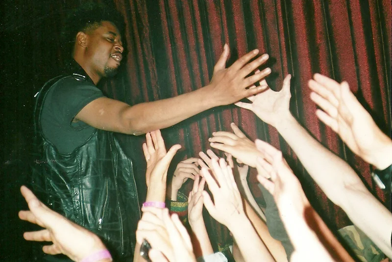 A performer reaching out to audience members during a concert or event, with multiple hands reaching towards him. music, editorial, album cover, photoshoot, conceptual, concept art