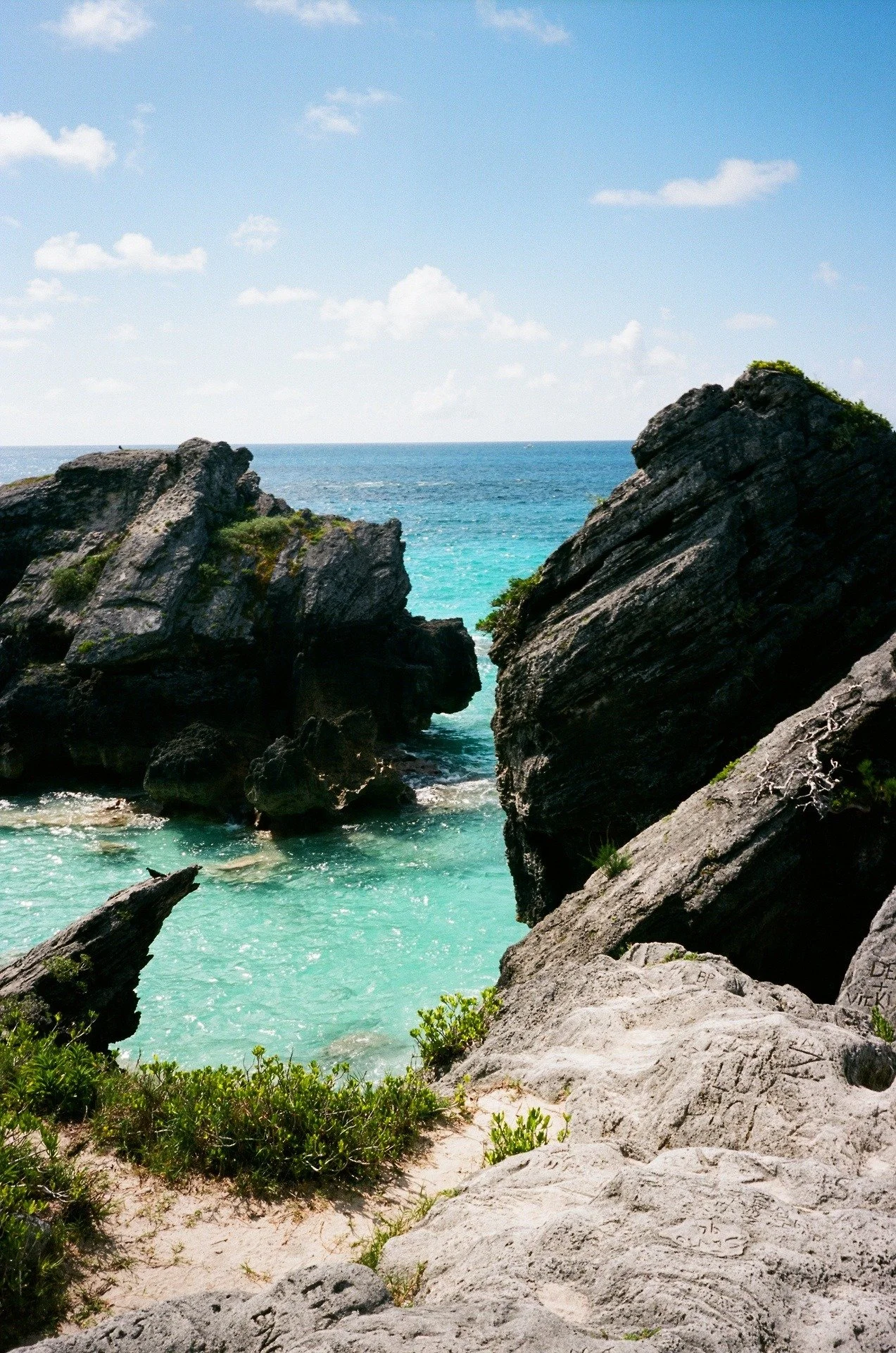 Sunlit rocky coastline with turquoise water and blue sky.