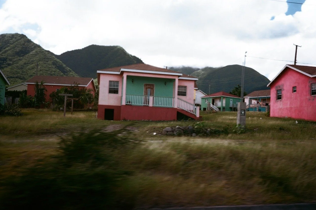 Colorful houses on a grassy hillside with mountains in the background and cloudy sky overhead.