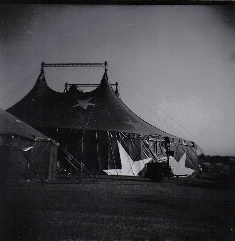 Black and white photo of a circus tent with star decorations, set up outdoors during dusk or nighttime.