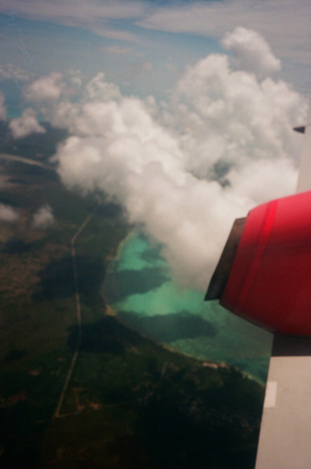 Aerial view of a large lake or reservoir with a dam, surrounded by green land, seen from an airplane window with part of the airplane wing visible.
