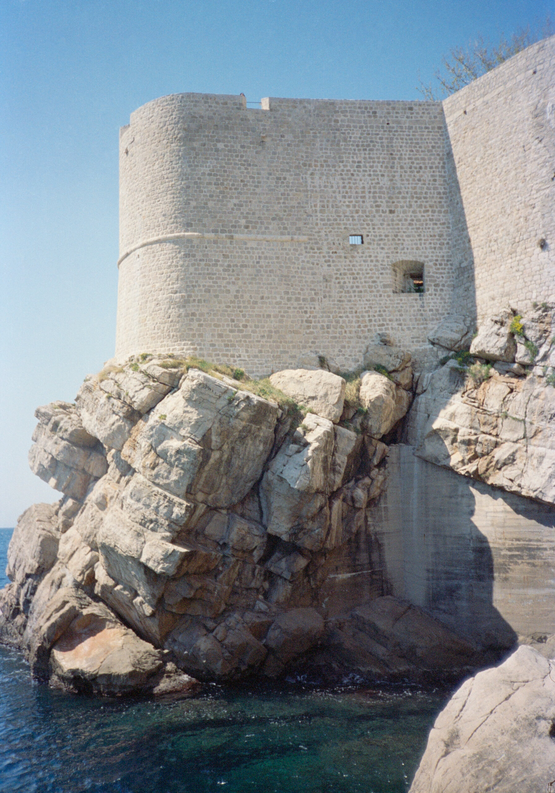 A stone fortress built on large rocky cliffs overlooking the sea under a clear blue sky.