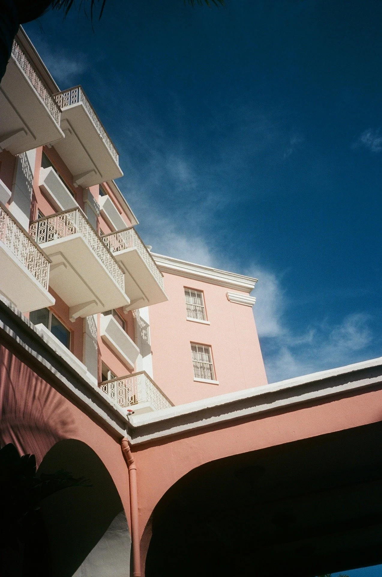 A pink building with white balconies and ornate railings, set against a bright blue sky.