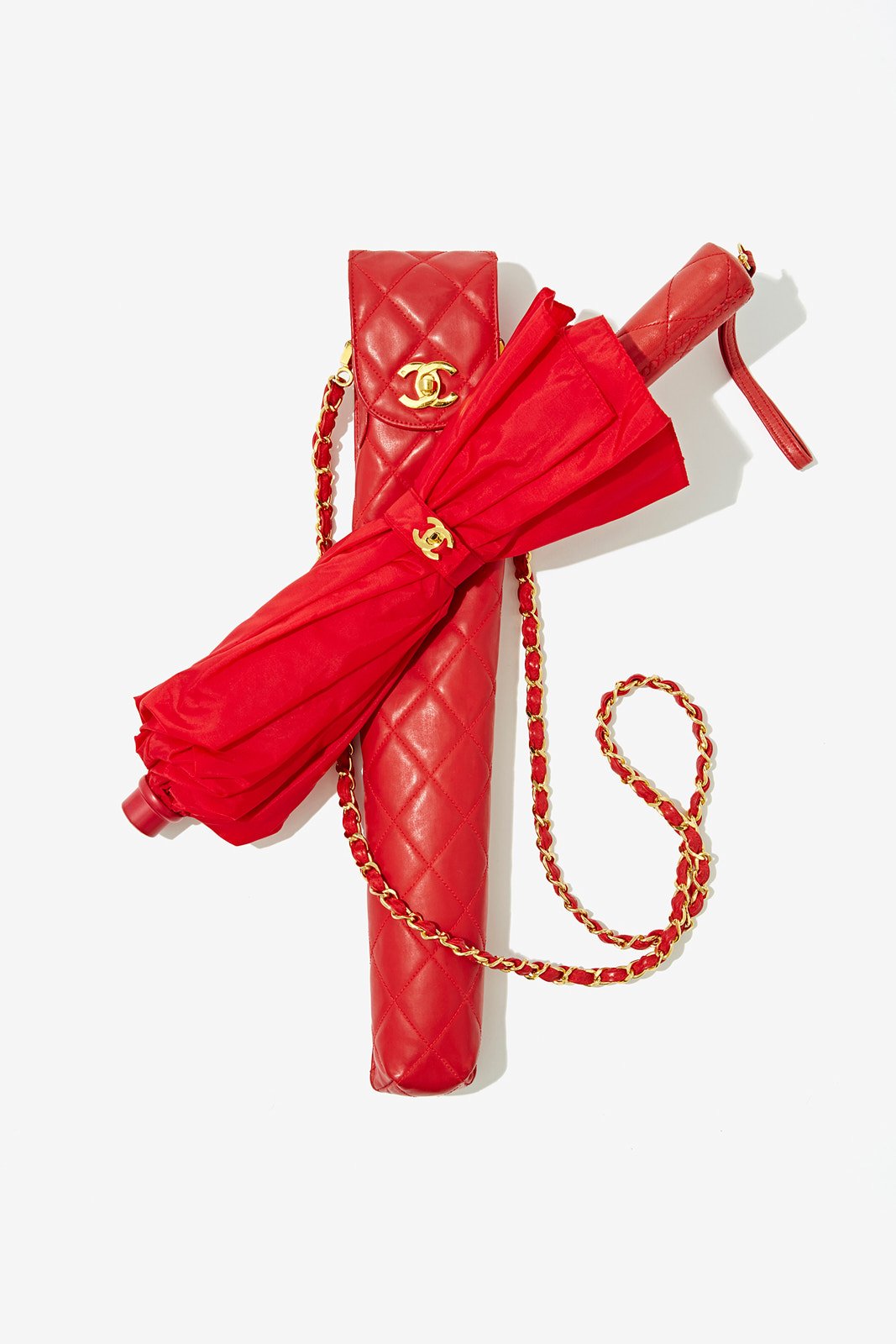 Red Chanel umbrella, quilted red Chanel purse, and a red Chanel raincoat with gold chain accents on a white background.