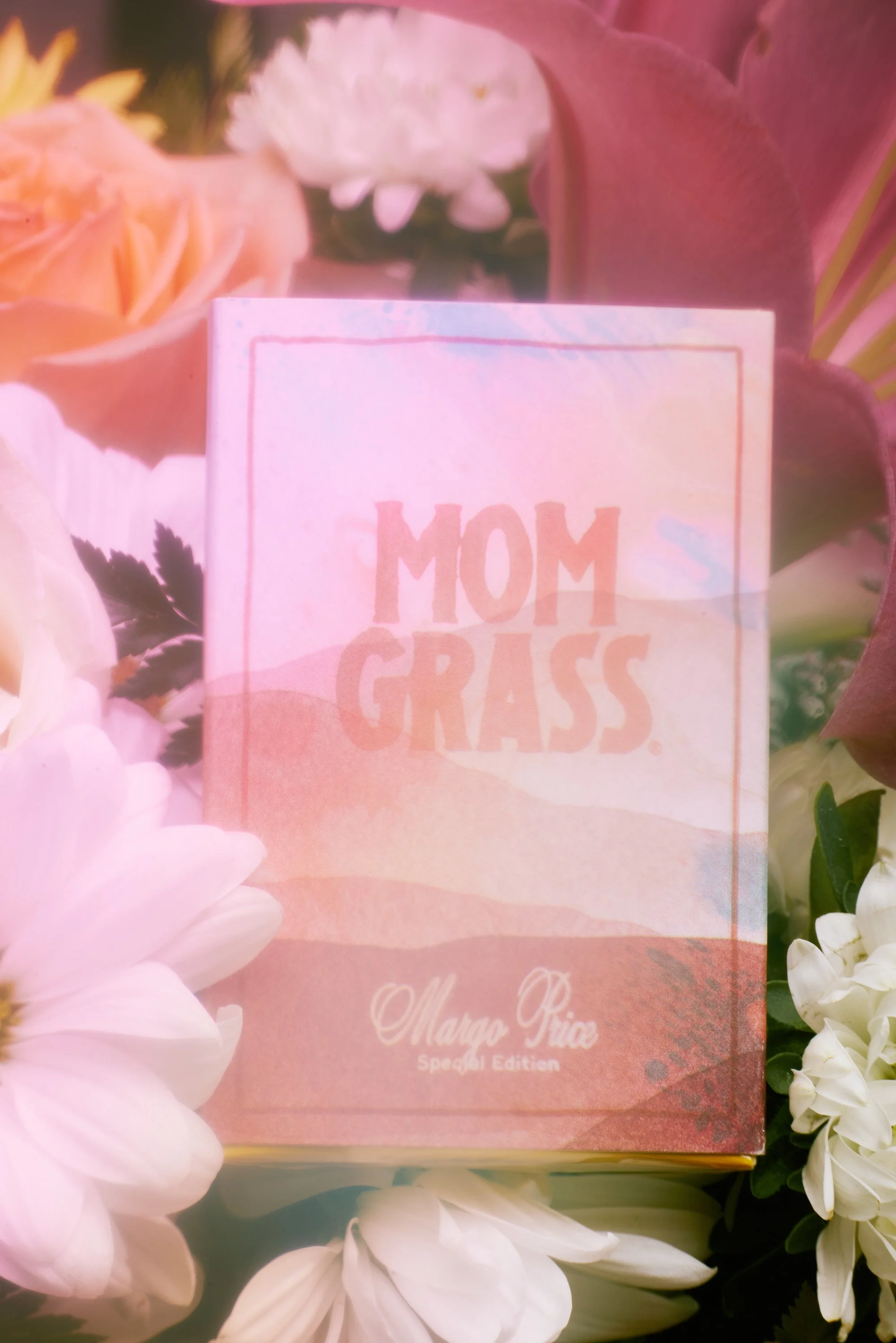 A pink book titled 'Mom Grass' by Marja Piia is surrounded by pink, white, and peach flowers.