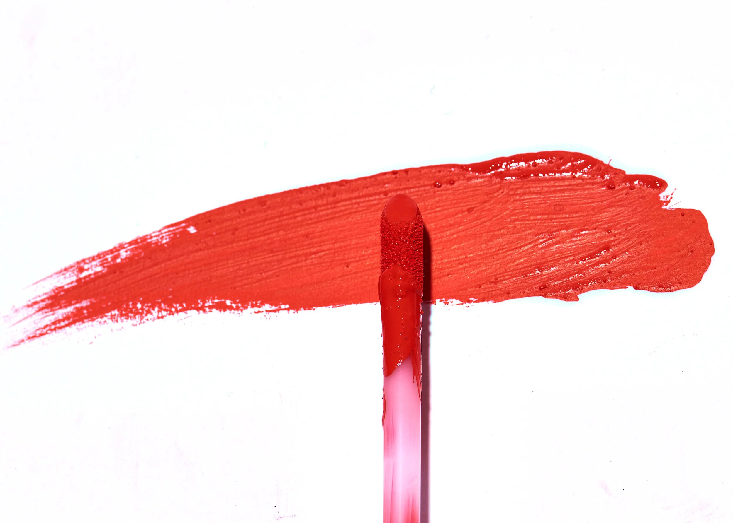 A pink applicator dipped in red lipstick, with a smear of red lipstick on a white background.